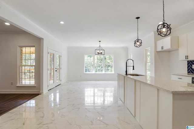 kitchen with french doors, light stone counters, sink, decorative light fixtures, and white cabinetry