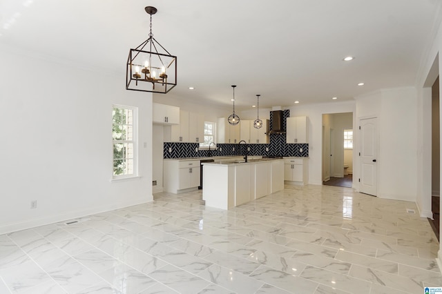 kitchen with white cabinetry, wall chimney exhaust hood, a kitchen island with sink, and decorative light fixtures