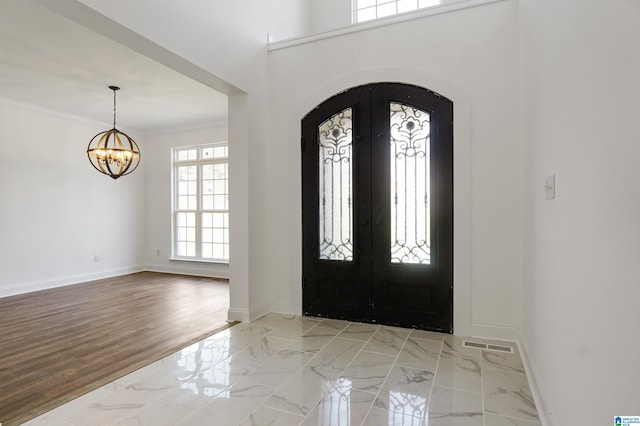 entryway with an inviting chandelier, crown molding, and french doors