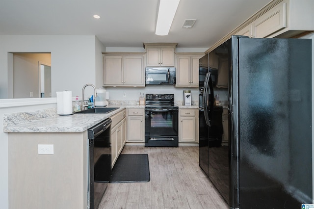 kitchen featuring black appliances, sink, light stone countertops, light wood-type flooring, and cream cabinetry