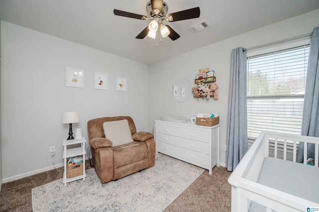 carpeted bedroom featuring ceiling fan and a nursery area