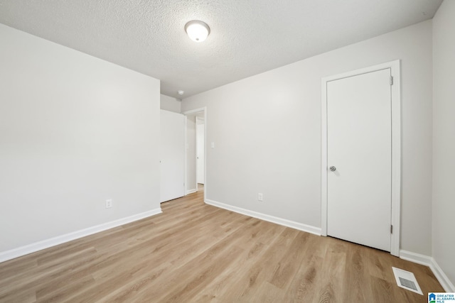 empty room with light wood-type flooring and a textured ceiling