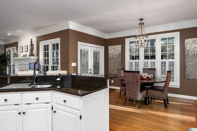 kitchen featuring french doors, light wood-type flooring, sink, white cabinetry, and hanging light fixtures