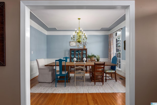 dining space with wood-type flooring, crown molding, and a chandelier