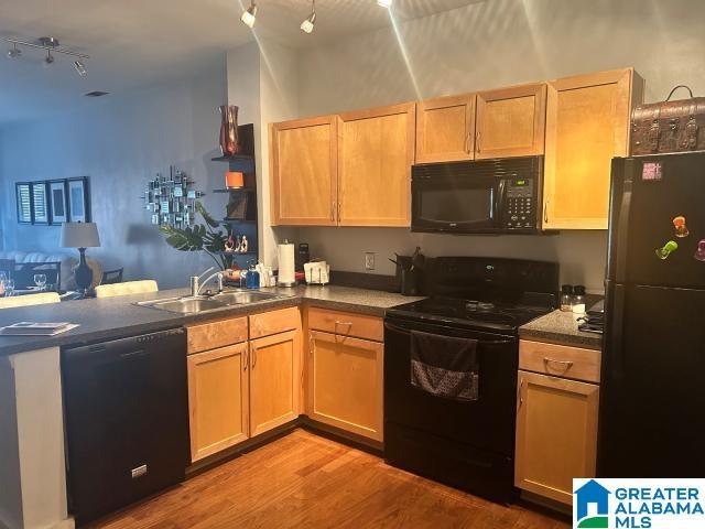 kitchen featuring kitchen peninsula, light brown cabinetry, sink, black appliances, and light hardwood / wood-style floors