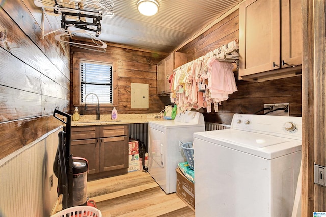 clothes washing area featuring cabinets, washing machine and dryer, wood walls, and sink