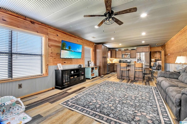 living room featuring light wood-type flooring, ceiling fan, and wood walls