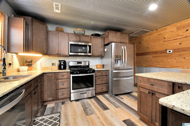 kitchen with wooden walls, sink, light stone counters, and appliances with stainless steel finishes