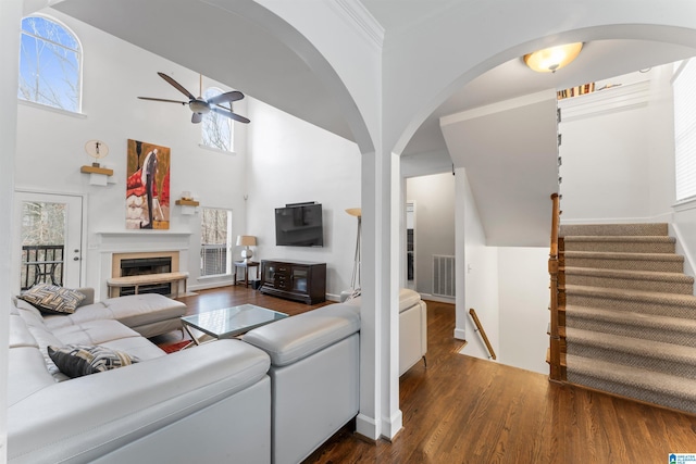 living room featuring a high ceiling, crown molding, ceiling fan, and dark wood-type flooring