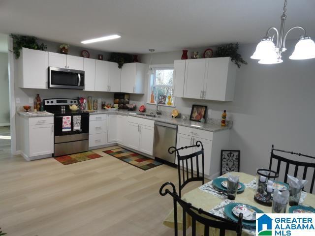 kitchen featuring appliances with stainless steel finishes, pendant lighting, sink, white cabinets, and light hardwood / wood-style flooring