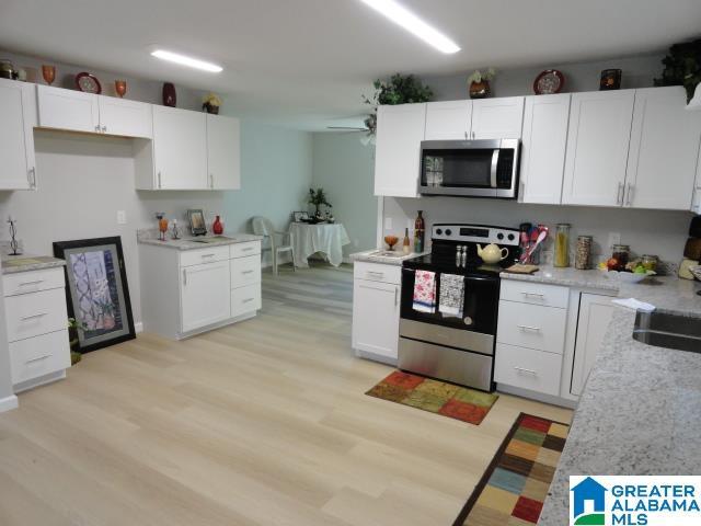 kitchen with stainless steel appliances, white cabinetry, ceiling fan, and light hardwood / wood-style flooring