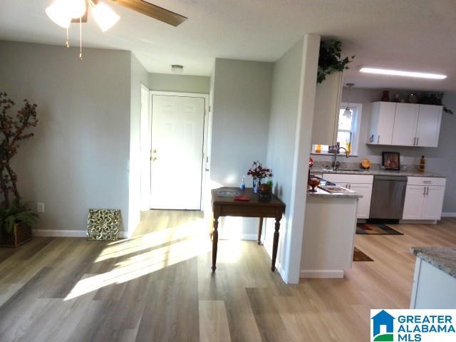 kitchen with sink, stainless steel dishwasher, white cabinets, and light hardwood / wood-style flooring