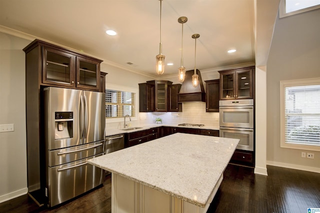 kitchen with a center island, premium range hood, sink, appliances with stainless steel finishes, and decorative light fixtures