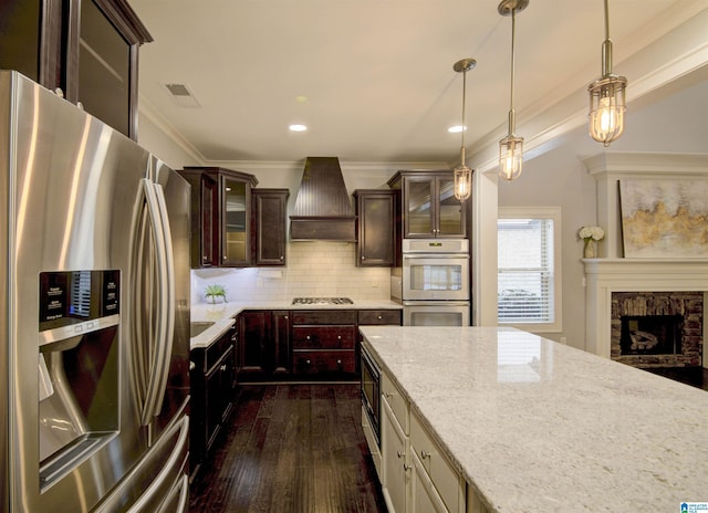 kitchen featuring a stone fireplace, backsplash, decorative light fixtures, custom range hood, and appliances with stainless steel finishes