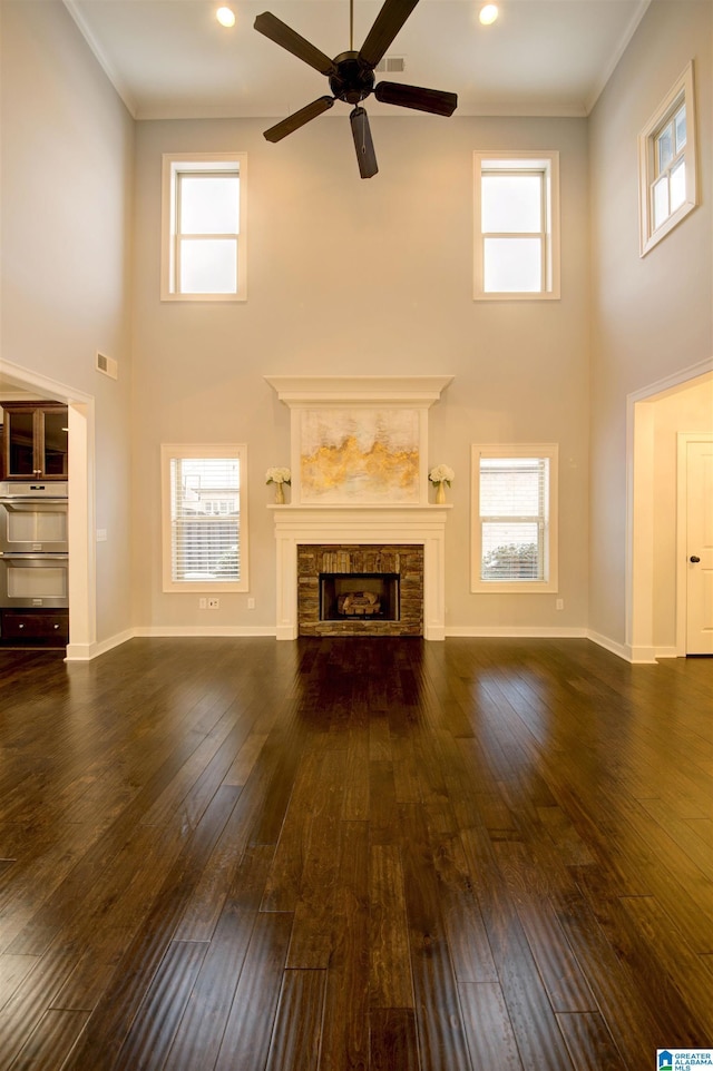 unfurnished living room featuring ceiling fan, a fireplace, a towering ceiling, and dark hardwood / wood-style floors