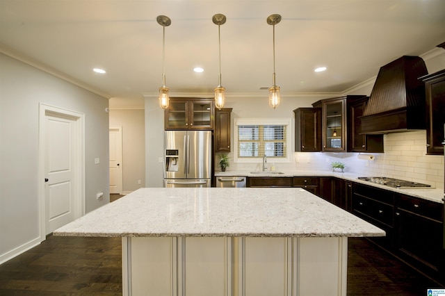 kitchen with appliances with stainless steel finishes, premium range hood, light stone counters, sink, and a center island