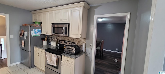 kitchen with appliances with stainless steel finishes, tasteful backsplash, light tile patterned flooring, a textured ceiling, and cream cabinets