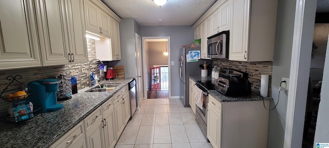 kitchen featuring a textured ceiling, stainless steel appliances, dark stone countertops, sink, and light tile patterned floors