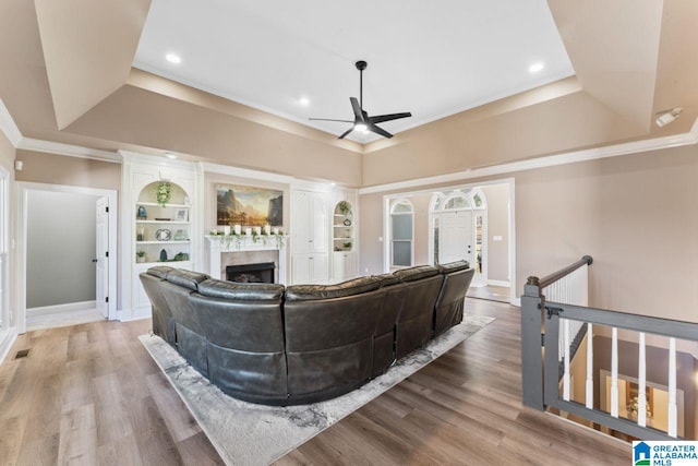 living room with wood-type flooring, a tray ceiling, built in features, and ceiling fan