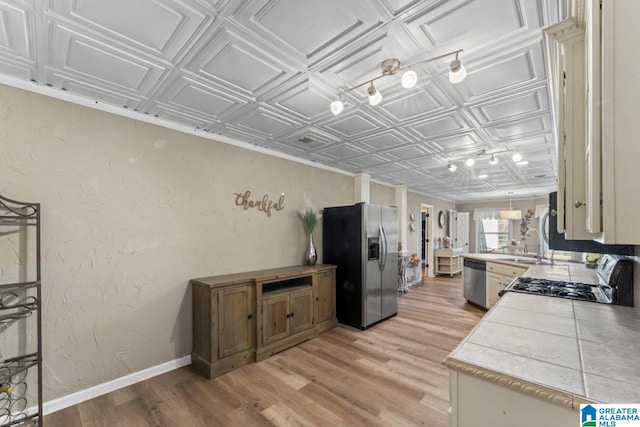 kitchen featuring tile counters, sink, stainless steel appliances, kitchen peninsula, and light wood-type flooring