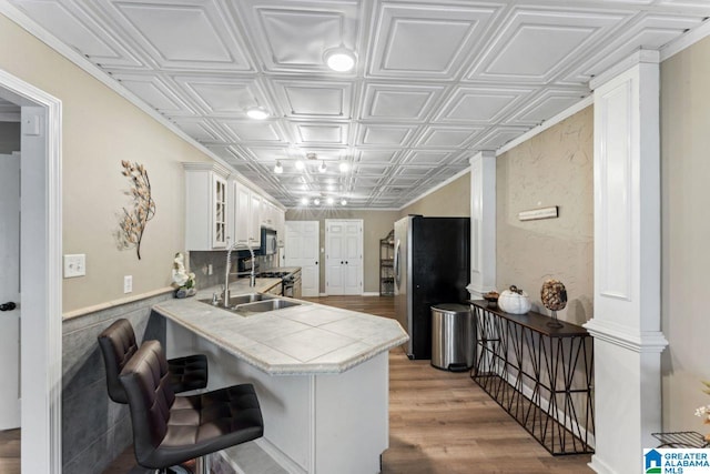 kitchen featuring kitchen peninsula, stainless steel fridge, a breakfast bar, sink, and white cabinetry