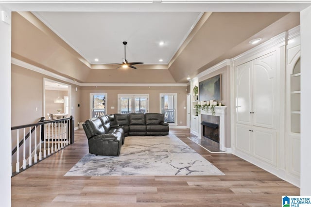 living room with ceiling fan, a raised ceiling, ornamental molding, and light hardwood / wood-style flooring