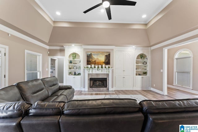 living room featuring a high end fireplace, built in shelves, light wood-type flooring, and ceiling fan