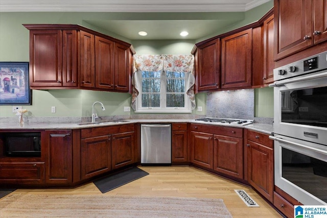 kitchen with appliances with stainless steel finishes, light wood-type flooring, tasteful backsplash, ornamental molding, and sink