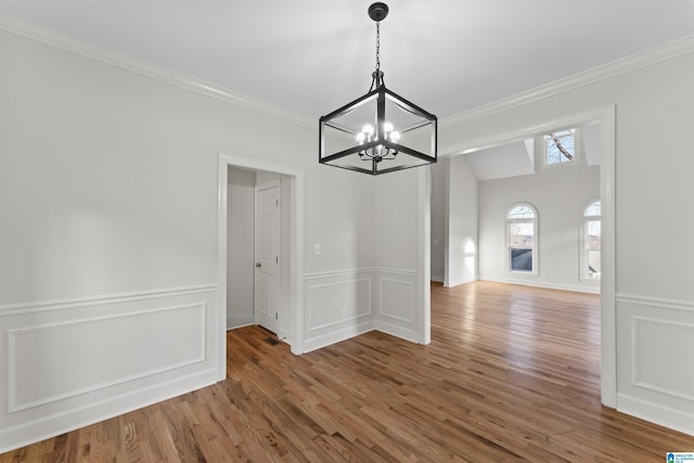 unfurnished dining area with wood-type flooring, crown molding, and an inviting chandelier