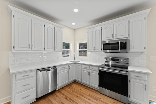 kitchen with sink, light wood-type flooring, stainless steel appliances, decorative backsplash, and white cabinets