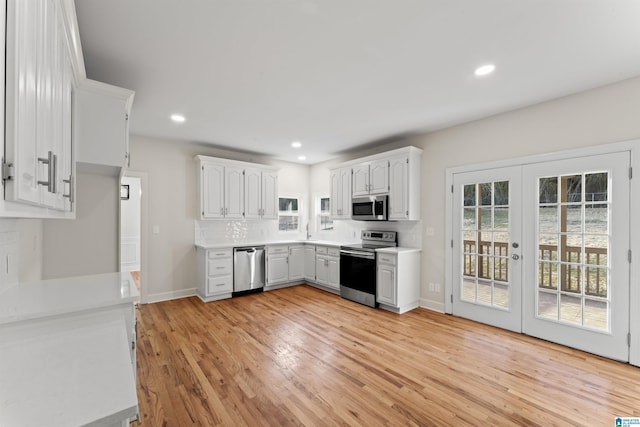 kitchen with appliances with stainless steel finishes, white cabinets, backsplash, and light hardwood / wood-style floors