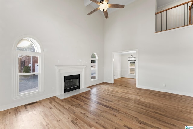 unfurnished living room with beam ceiling, ceiling fan, light wood-type flooring, and high vaulted ceiling