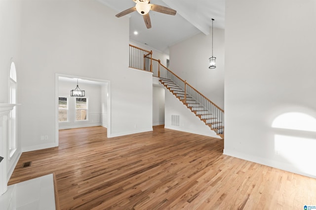 unfurnished living room featuring ceiling fan with notable chandelier, beam ceiling, high vaulted ceiling, and hardwood / wood-style floors