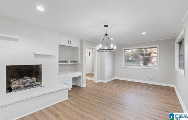 unfurnished dining area featuring light wood-type flooring, a brick fireplace, ornamental molding, and a notable chandelier