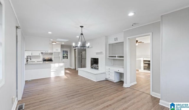 unfurnished living room with ceiling fan with notable chandelier, light hardwood / wood-style floors, ornamental molding, and sink