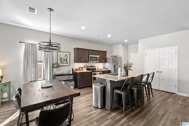 kitchen with appliances with stainless steel finishes, backsplash, sink, a center island with sink, and a chandelier