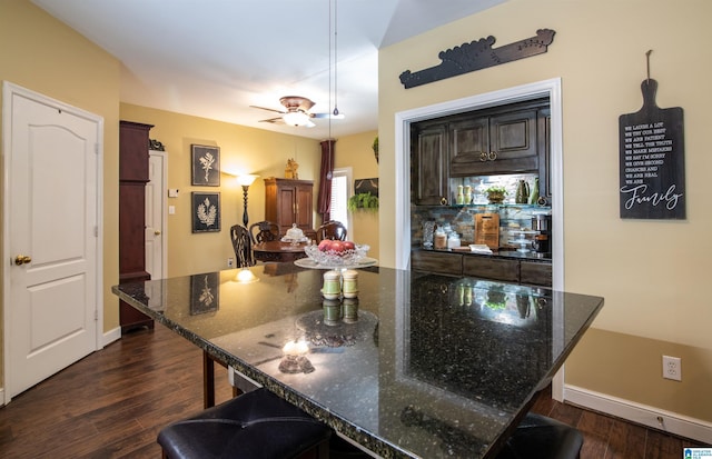 kitchen featuring decorative light fixtures, a kitchen bar, dark stone countertops, and dark wood-type flooring