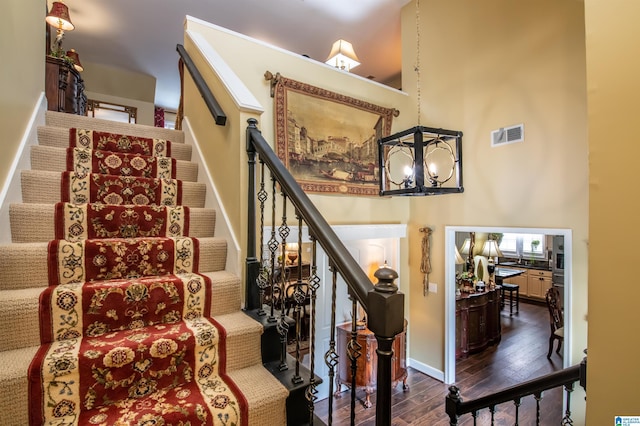 stairway featuring wood-type flooring, a high ceiling, and a chandelier