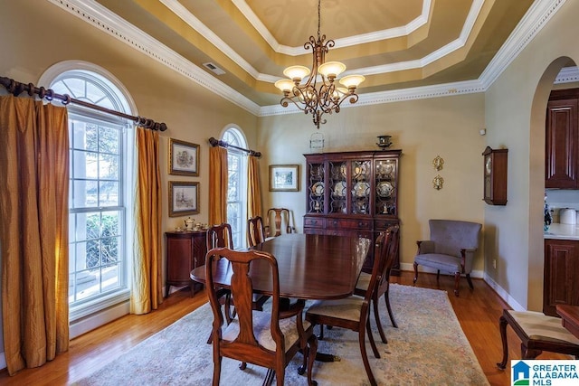 dining space with a chandelier, ornamental molding, a tray ceiling, and light hardwood / wood-style floors