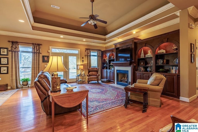 living room with ceiling fan, crown molding, light hardwood / wood-style flooring, and a tray ceiling