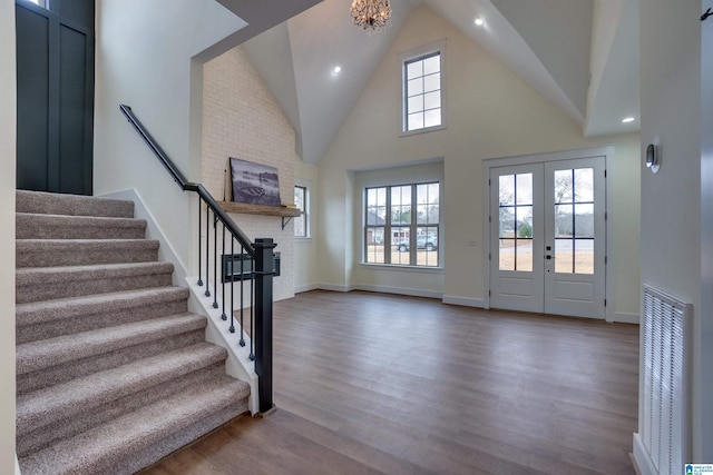 foyer featuring french doors, a towering ceiling, hardwood / wood-style flooring, and an inviting chandelier