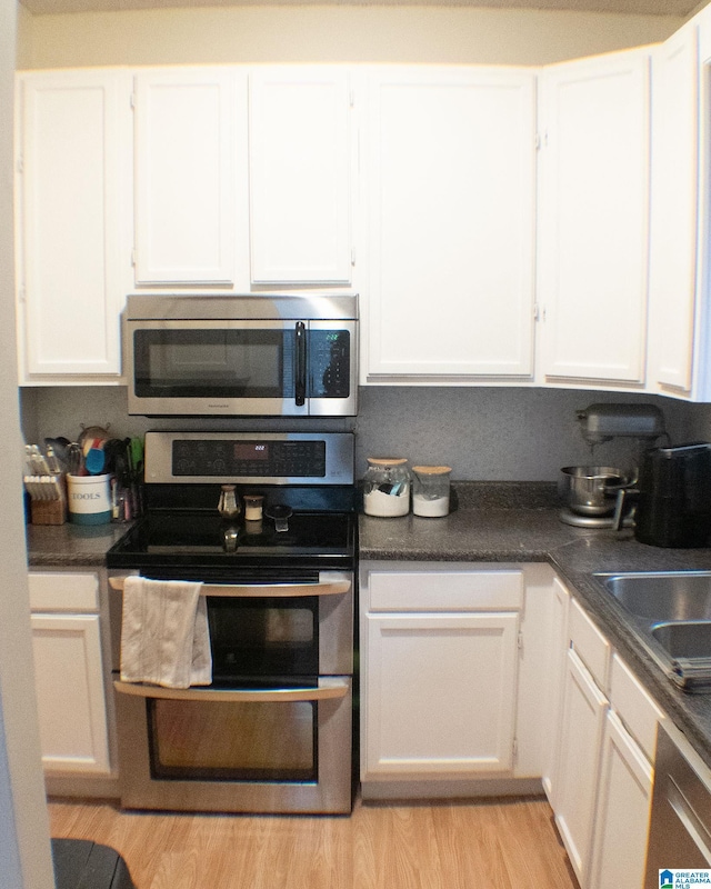 kitchen with light wood-type flooring, stainless steel appliances, white cabinetry, and sink