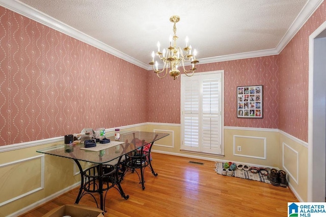 dining space featuring crown molding, wood-type flooring, a textured ceiling, and an inviting chandelier