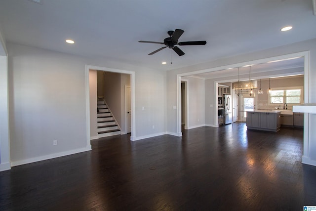 unfurnished living room with sink, dark wood-type flooring, and ceiling fan with notable chandelier