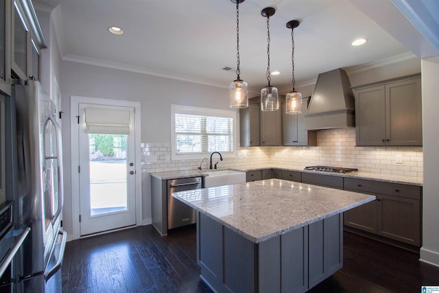 kitchen featuring appliances with stainless steel finishes, custom range hood, sink, pendant lighting, and a center island