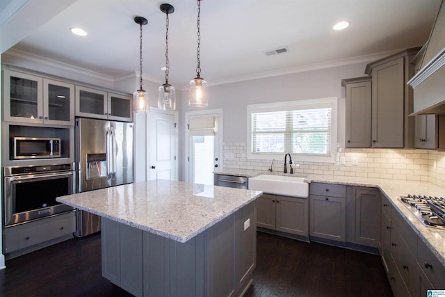 kitchen with light stone countertops, a kitchen island, stainless steel appliances, and decorative light fixtures