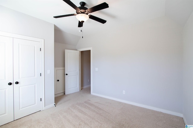 unfurnished bedroom featuring ceiling fan, a closet, light carpet, and vaulted ceiling