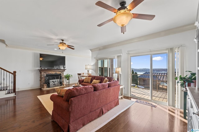 living room with dark hardwood / wood-style floors, ornamental molding, ceiling fan, and a stone fireplace