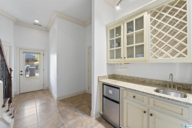 kitchen with light stone countertops, crown molding, stainless steel refrigerator, cream cabinetry, and sink