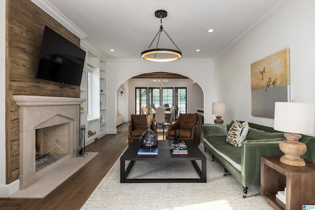 living room with an inviting chandelier, built in features, crown molding, and hardwood / wood-style floors